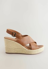 Brown leather wedge sandal with crossed straps and adjustable ankle buckle, featuring a braided jute platform sole.