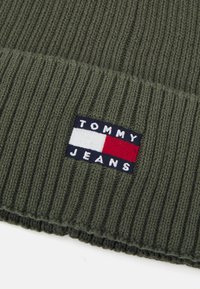 Gorro de punto acanalado verde con una superficie texturizada y un parche de marca que dice "TOMMY JEANS" en colores blanco, navy y rojo.