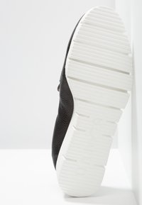 Baskets noires avec une tige texturée. Semelle en caoutchouc blanc dotée de rainures horizontales pour une meilleure adhérence. Design simple avec un minimum de détails.