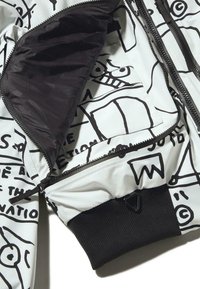 Könnyű bomber dzseki fehér alapon fekete absztrakt mintákkal. Fekete bordázott mandzsetták és belső bélés. Cipzáras zsebek.