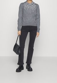 Grå stickad tröja med dekorativt vitt pärlmönster, kombinerad med svarta utsvängda jeans och kraftiga svarta ankelskor. Håller en svart handväska.