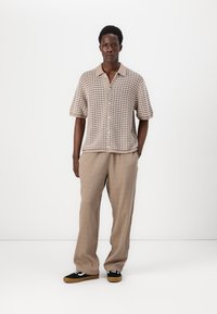 Beige short-sleeve shirt with a textured pattern and collar, paired with light trousers and black sneakers featuring white accents.