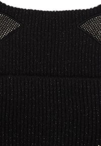 Pull en tricot noir avec des côtes verticales, mettant en avant des panneaux texturés avec des accents scintillants sur les épaules. Tissu doux et chaud.