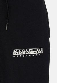 Schwarze Jogginghose aus einem Baumwollmischgewebe, mit einem weißen Aufdruck des Logos "NAPAPIJRI geographic" auf dem linken Oberschenkel und einem Kordelzugbund.