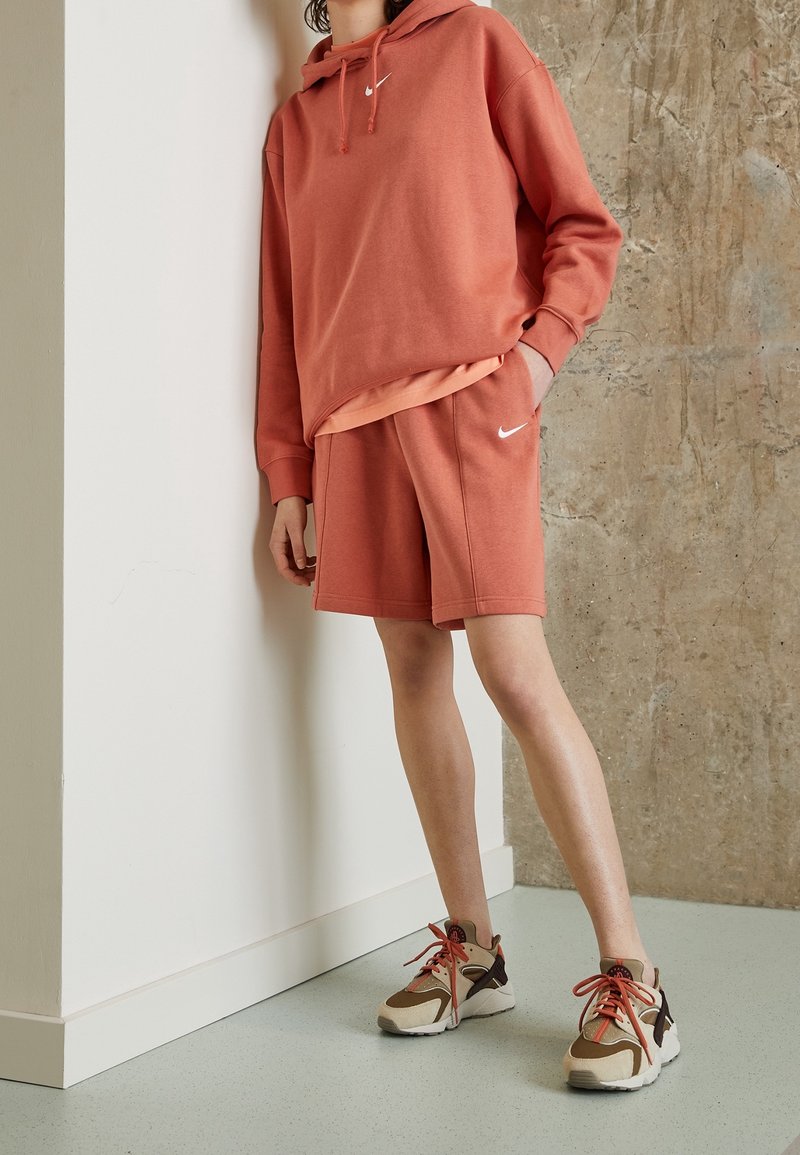 Coral hoodie with front pocket and drawstrings, paired with matching shorts. Wearing beige and brown sneakers with red laces.