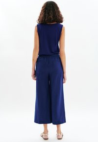 Marineblauw mouwloos topje, gecombineerd met wijde broek met elastische tailleband en twee achterzakken, gemaakt van lichtgewicht stof.