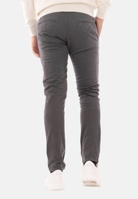 Pantaloni in cotone grigi con fit slim, dotati di tasche posteriori, cuciture sottili e con orlo usurato, abbinati a sneaker bianche.