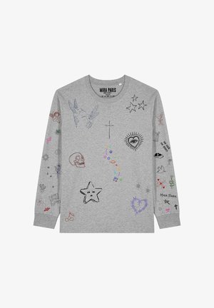 Giovane donna con capelli castani raccolti in una coda di cavallo che indossa una felpa grigia decorata con piccoli disegni e simboli multicolori in stile schizzo.