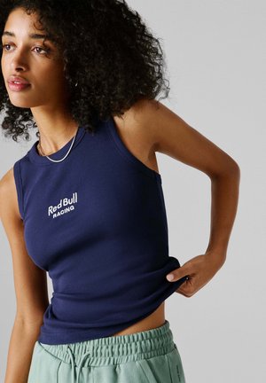 Tumesinine soonikkoes tank top, millel on "Red Bull Racing" tikand, kombineeritud helesiniste elastse vöökohaga pükstega. Sile tekstuur, varrukateta disain.