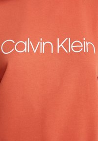 Felpa in cotone arancione con un grande logo bianco "Calvin Klein" centrato sul petto, con una texture liscia e scollo rotondo.