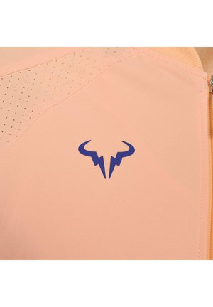 Perzikkleurig sporttop met mesh-details, voorzien van een blauw logo. Gladde textuur met subtiele perforaties voor ademend vermogen.