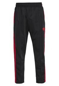 Pantalon de sport noir avec des bandes rouges sur les côtés, une taille élastique et un petit logo. Confectionné en tissu lisse et léger, avec deux poches latérales.