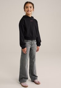 Črna skrajšana kapuca z rdečim napisom, sivi široki kavbojke in roza tenisice. Gladka tekstura, sproščen dizajn.