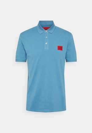 Polo bleu clair en coton. Comprend un col, trois boutons, et un patch logo rectangulaire rouge sur la poitrine gauche.