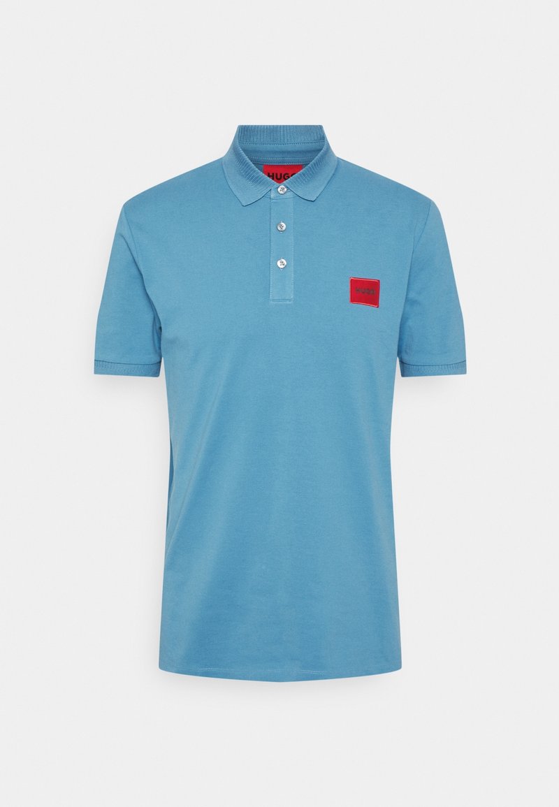 Polo bleu clair en coton. Comprend un col, trois boutons, et un patch logo rectangulaire rouge sur la poitrine gauche.