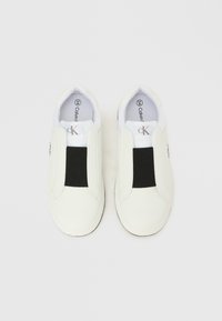 Λευκά παπούτσια slip-on με μαύρα ελαστικά πάνελ, λείο δερμάτινο εξωτερικό, στρογγυλεμένη μύτη και επένδυση με το λογότυ πο. Απλός και μοντέρνος σχεδιασμός.