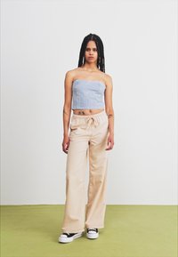 Light blue denim cropped top with vertical seams, paired with cream-colored wide-leg pants. Black and white sneakers complete the look.