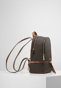 Sac à dos en toile monogramme marron avec des accents en cuir beige, double fermeture éclair, bretelles réglables et un fond plat pour plus de stabilité.