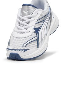 Baskets de sport blanches en maille avec des accents bleus, détails en argent texturé, fermeture à lacets et semelle en caoutchouc flexible. Présente un motif distinct.