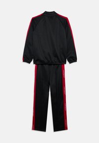 Chándal negro con franjas rojas en las mangas y las piernas, con texto blanco repetido "JORDAN" en las franjas, extendido sobre una superficie plana.