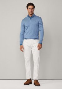 Svijetloplavi pleteni pulover sa zip ovratnikom, kombiniran sa bijelim hlačama i smeškim nubuk cipelama, s tamnoplave akcentima na manžetama.