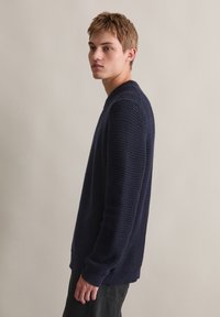 Marineblauer strukturierter Pullover mit Rundhalsausschnitt und langen Ärmeln, ausgestattet mit einem gerippten Saum. Das Waffelmuster verleiht dem Design Tiefe.