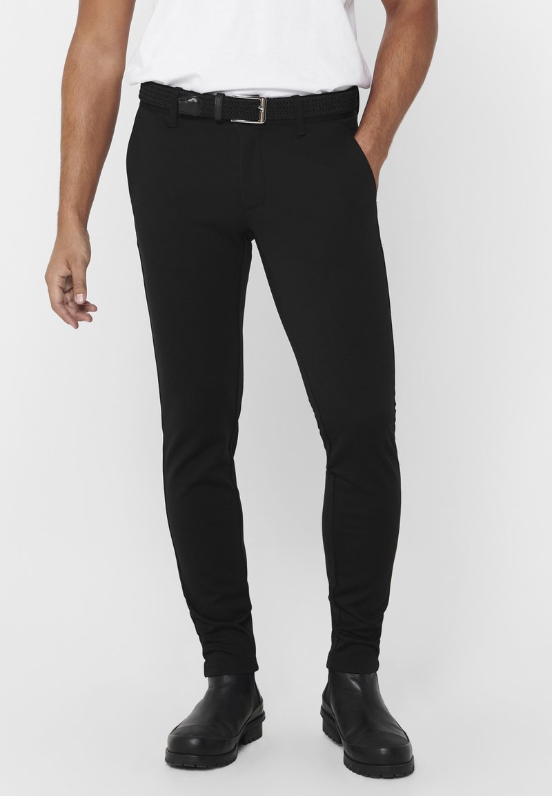 Zwarte slim-fit broek van rekbaar materiaal, met zijzakken, een gladde textuur en een gevlochten zwarte riem met een zilveren gespsluiting.