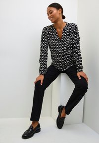 Blusa a righe in bianco e nero con scollatura a V, maniche lunghe e vestibilità morbida, abbinata a pantaloni skinny neri e mocassini neri.