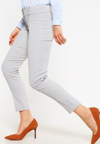 Ljusgrå tapered byxor med en slät textur, medelhög midje, och sidfickor, i kombination med bruna spetsiga klackar.