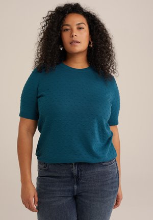 Maglione in maglia corto a maniche corte color teal con un motivo a pois testurizzato; scollatura rotonda; abbinato a jeans blu scuro per un look casual.