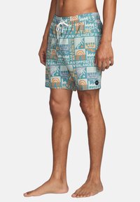 Simshorts i teal med livliga mönster som inkluderar text och former. Elastisk midja med snörning. Tillverkade av lätt material.