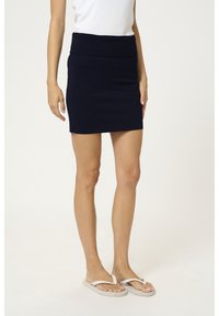 Námořnická modrá pletená mini sukně se širokým elastickým páskem, s hladkou texturou a přiléhavým střihem, doplněná o světle sandály.