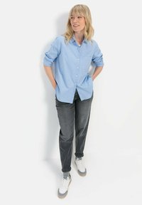 Lichtblauw overhemd met opgerolde mouwen, grijze broek en witte sneakers. Het overhemd heeft een enkele borstzak en een lose fit.