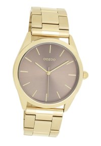 Montre-bracelet en métal doré avec un boîtier rond, un cadran dégradé marron, des indices horaires minimalistes et un bracelet en métal relié. Nom de la marque "OOZOO" visible.