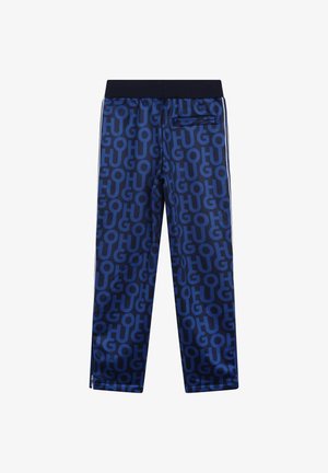 Granatowe dresy wykonane z błyszczącej tkaniny z powtarzającym się wzorem logo. Elastyczny pas, boczne paski oraz kieszeń z zamkiem błyskawicznym z tyłu.