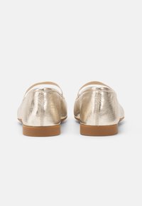 Metallic gold ballerina flats with elastic ankle strap, round toe, smooth texture, and a flexible brown sole. Clean, minimalist design.