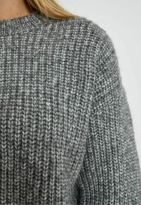Chunky grijze gebreide sweater met een geribbelde textuur in verschillende tinten, een ronde halslijn en iets verlaagde schouders.