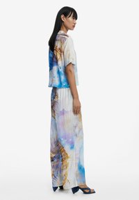 Multikleurige two-piece outfit met een T-shirt met korte mouwen en losse broeken. Gemaakt van lichte stof met een blauw, wit en goud patroon.