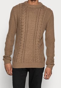 Maglione lavorato a maglia marrone con un motivo testurizzato e cavi alti. Collo e polsini a costine, realizzato con filato spesso per maggiore calore.
