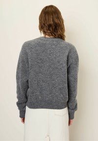 Sivana pletena jopica s sproščenim krojem, okroglo izrezano ovratnikom in rebrastim robom. Mehka tekstura, dolgi rokavi in subtilne pike v materialu.