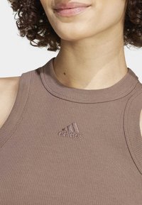 Brown ribbed sleeveless top with a high neckline and embroidered Adidas logo on the chest. Smooth texture with a fitted design.