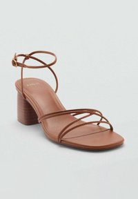 Brown heeled sandals with thin straps, a square toe, and a block heel. Made of smooth leather with a matte finish. Buckle closure detail.