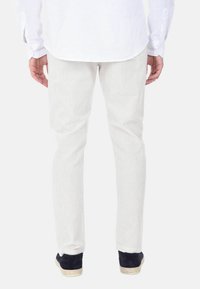 Pantaloni in cotone bianco a coste con una vestibilità aderente, vita elastica e una leggera texture. Abbinati a sneakers scure con suola chiara.
