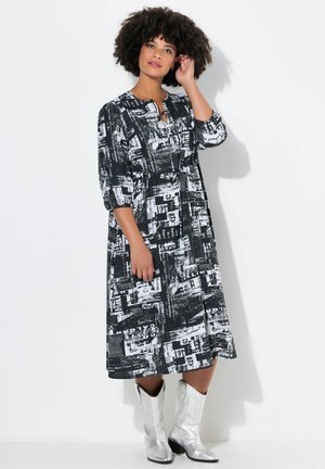 Schwarz-weiß bedrucktes Kleid mit lockerem Schnitt, knielang, mit rundem Halsausschnitt, halben Ärmeln und einem Bindegürtel. Getragen mit silbernen Stiefeln.