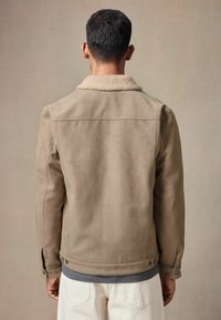Jachetă din suede bej cu un guler moale din blană, croială ajustată, mansete cu butoni și capse laterale. Textură netedă cu elemente de design minimalist.