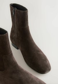 Bruine suède enkellaarsjes met een gladde textuur, puntige neus, lage blokhak en zijritssluiting. Eenvoudig en elegant ontwerp.