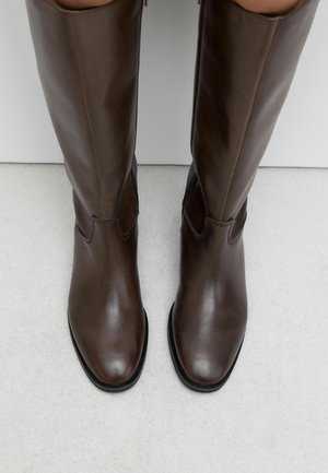 Brown leather knee-high boots with a sleek design, pointed toe, and subtle stitching detail along the upper. Flat soles.