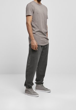 Grau T-Shirt mit kurzen Ärmeln, kombiniert mit dunkelgrauen, locker sitzenden Hosen und hellgrauen High-Top-Sneakern. Die Materialien wirken weich und glatt.