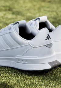 White athletic sneakers with smooth synthetic material, textured accents, three tonal stripes, and a grey rubber sole.