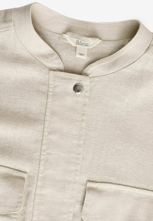 Beige Leinenhemd mit Rundkragen, zentraler Druckknopfverschluss und zwei vorderen Taschen. Hat eine subtile Textur und ein minimalistisches Design.